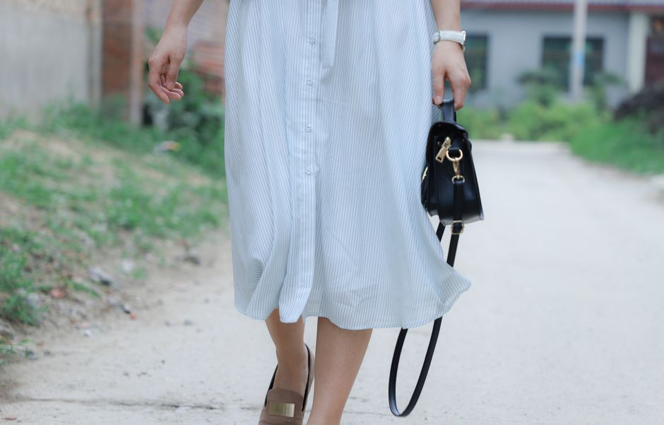 Woman walking outdoors in a casual summer dress with a black handbag.