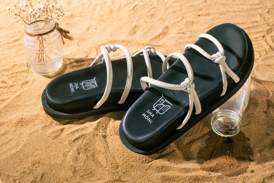 Trendy black sandals with white straps displayed on sand, perfect for summer fashion.