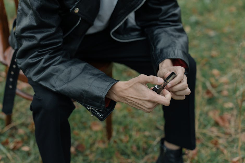A person in a leather jacket holding a lighter while sitting outdoors on grass.