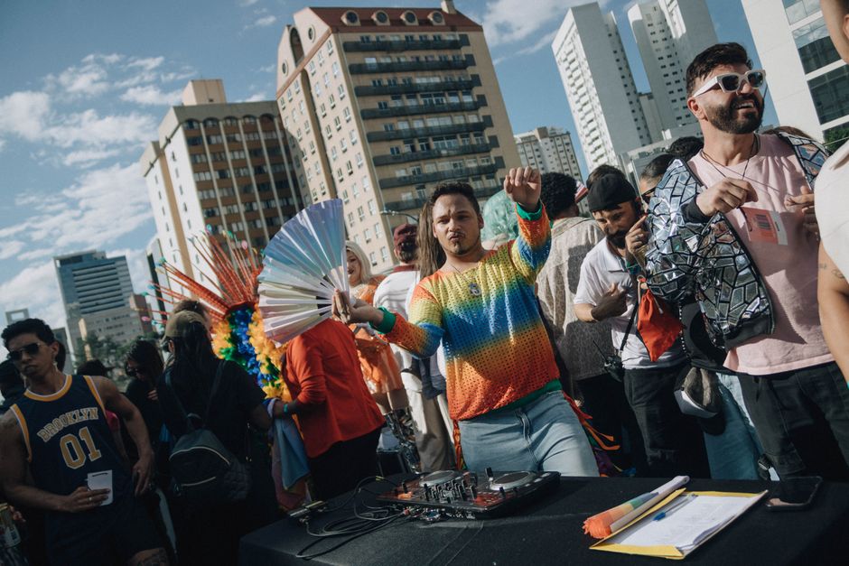A lively street parade featuring a DJ in colorful attire, surrounded by festive participants.