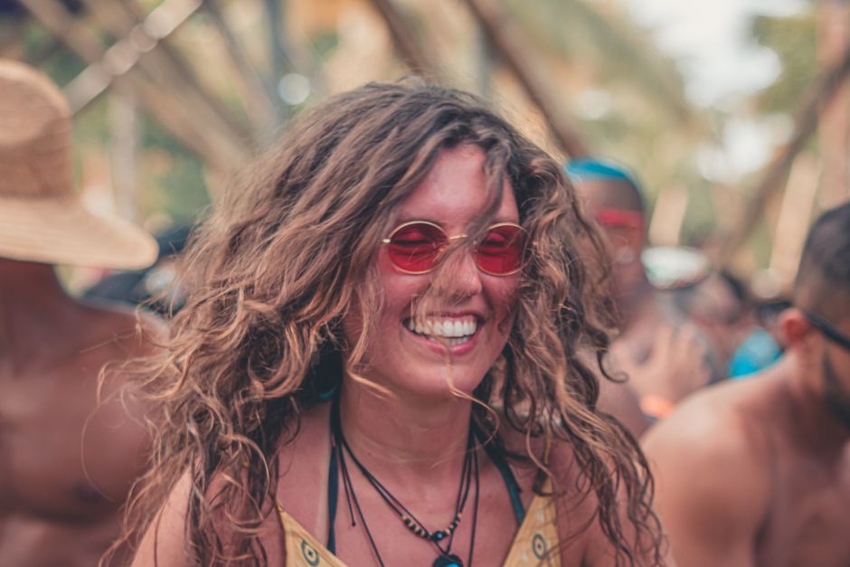 Smiling woman wearing red sunglasses at a lively outdoor festival in summer.