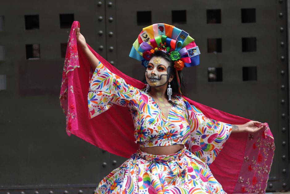 A vibrant Day of the Dead dancer showcases traditional Mexican attire with colorful makeup and floral headpiece.