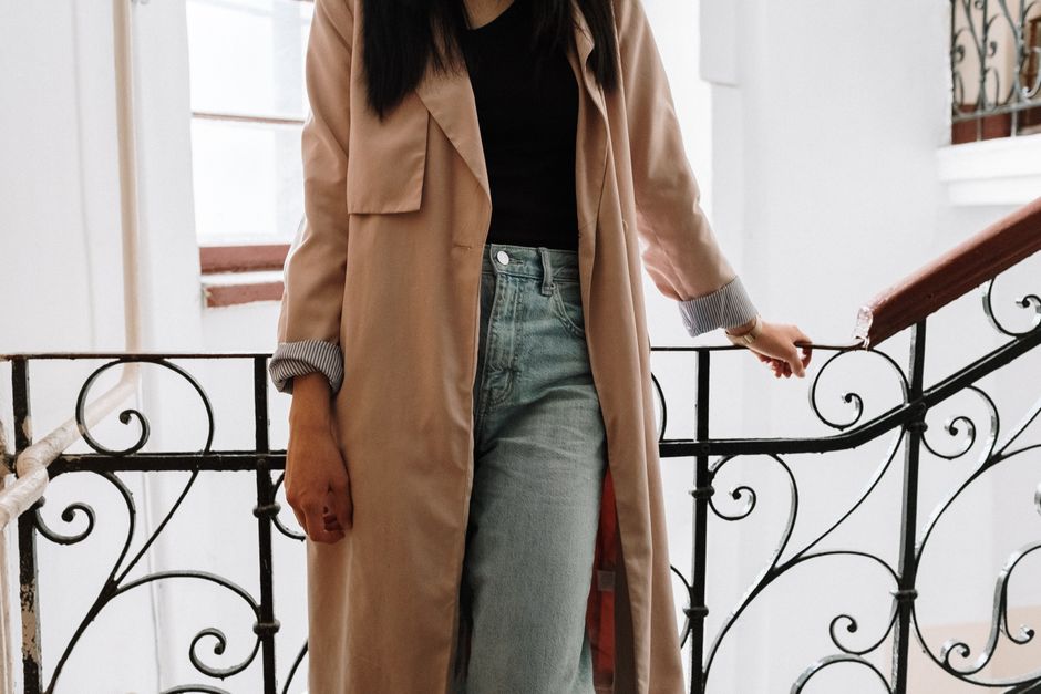 A fashionable woman in jeans and a coat stands on a vintage staircase with wrought iron railings.