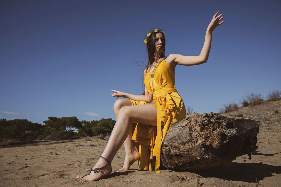 A young woman in a fashionable yellow dress poses gracefully on a sandy beach.