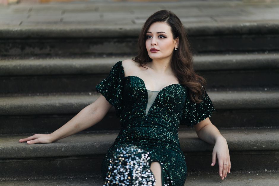 A stylish woman in a green sequined dress posing elegantly on stone steps outdoors.
