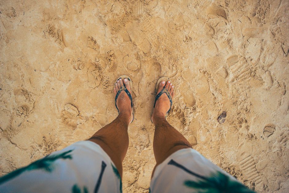 Top view of legs in flip-flops on sandy beach, capturing summer vibes and beachwear style.