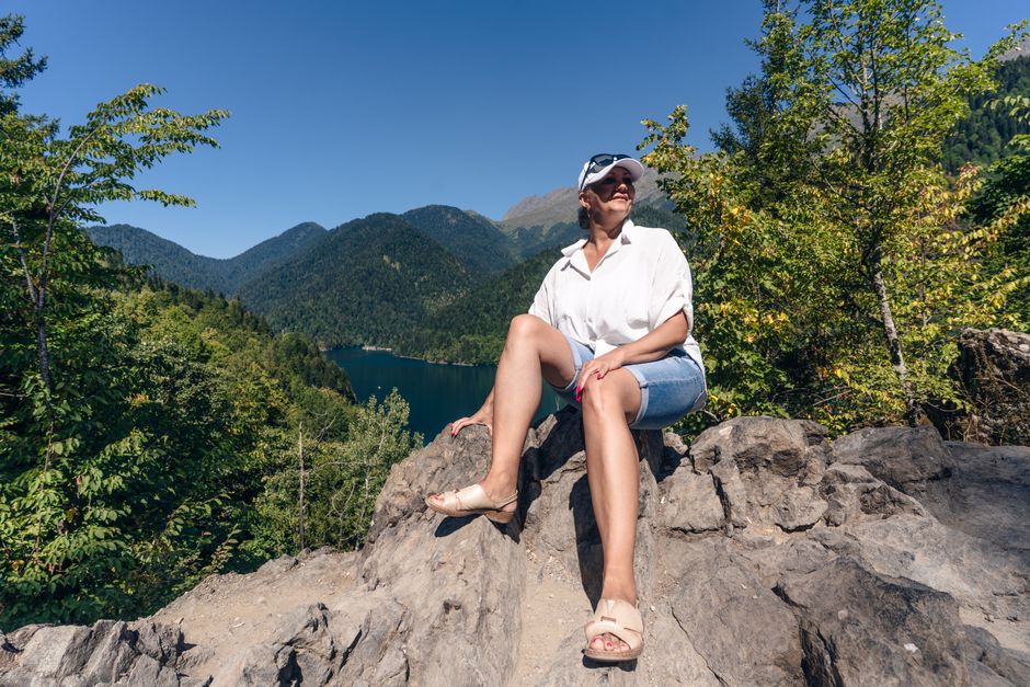 Smiling woman on rock overlooking the beautiful lake in Gagra. Perfect for travel and adventure themes.