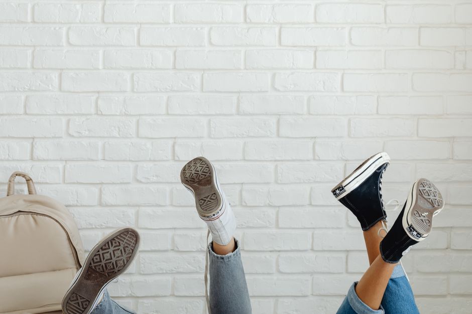 Three feet in sneakers raised against a stylish white brick wall, showcasing casual fashion and youthful vibe.