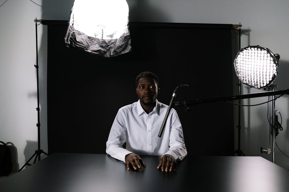 Man in a podcast studio sitting at a table with microphone and lighting equipment.