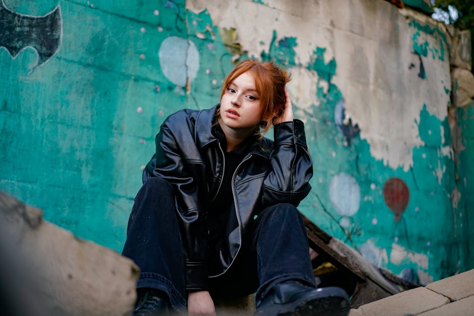 A young woman in a leather jacket poses against a colorful graffiti wall, showcasing urban fashion.