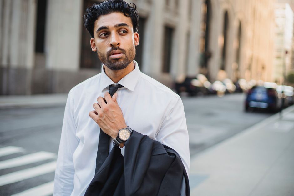 Young businessman in white shirt holding jacket on city street.
