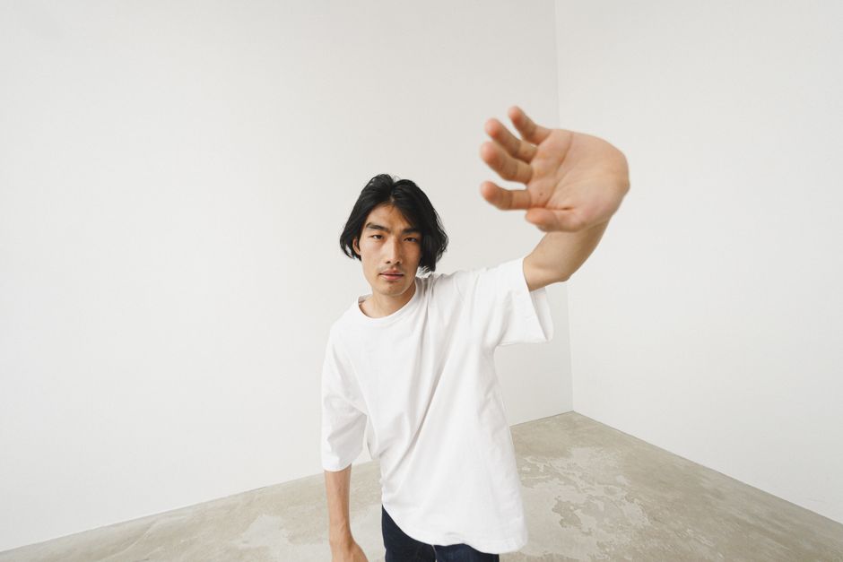 High angle portrait of a man in a white shirt reaching forward in a minimalist setting.
