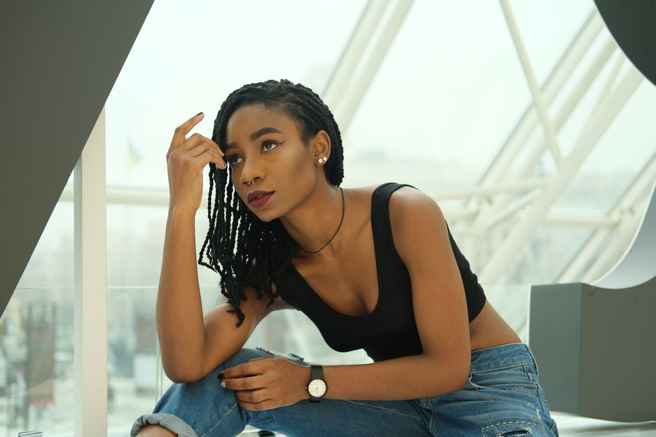 A stylish young woman in casual attire poses thoughtfully in a contemporary indoor setting.