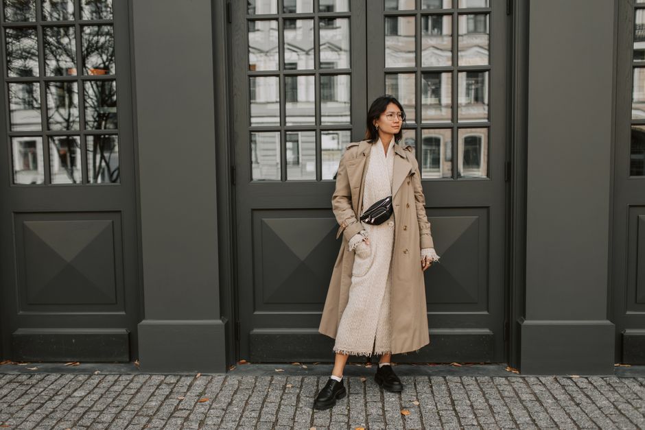 A fashionable woman poses confidently in a trench coat against an urban backdrop, showcasing street style.