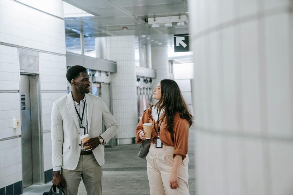African American man and Caucasian woman talking with coffee in a subway station, emphasizing communication and connection.