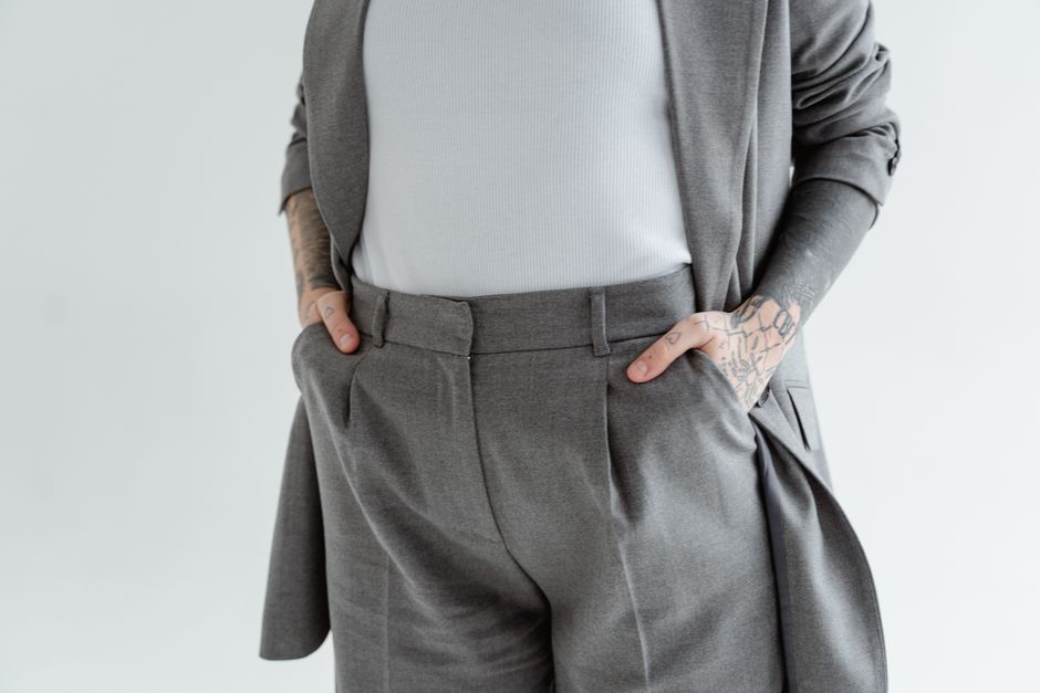 Close-up of a person in a gray suit with tattooed arms and hands in pockets.