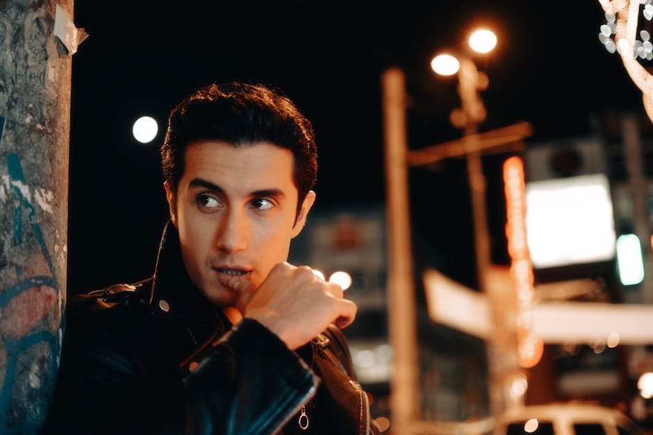 Stylish man wearing leather jacket in urban night cityscape, exuding elegance and confidence.