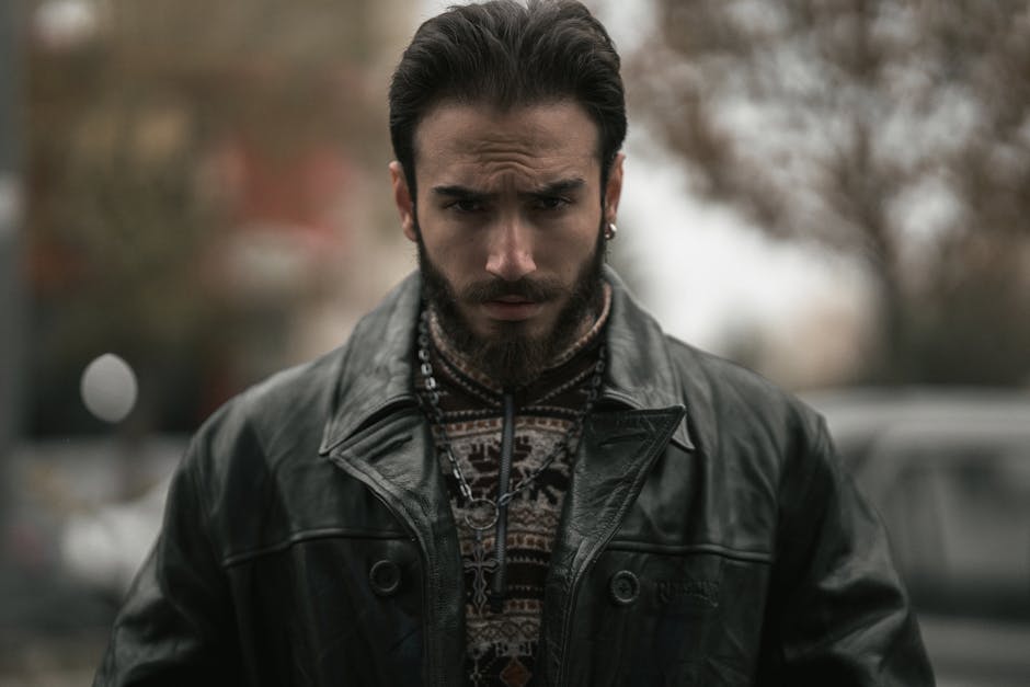 Portrait of a fashionable man in a leather jacket with a focused expression, outdoors.