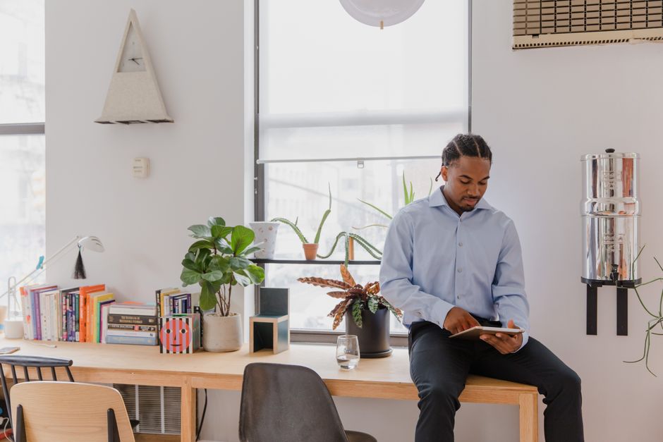 Man in blue shirt using tablet in modern indoor workspace with books and plants.