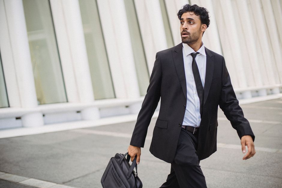 Confident businessman in corporate attire walking outside with a briefcase.