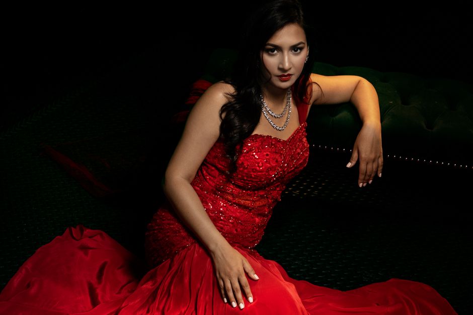 Sophisticated woman in a red gown and diamond necklace sitting elegantly indoors.