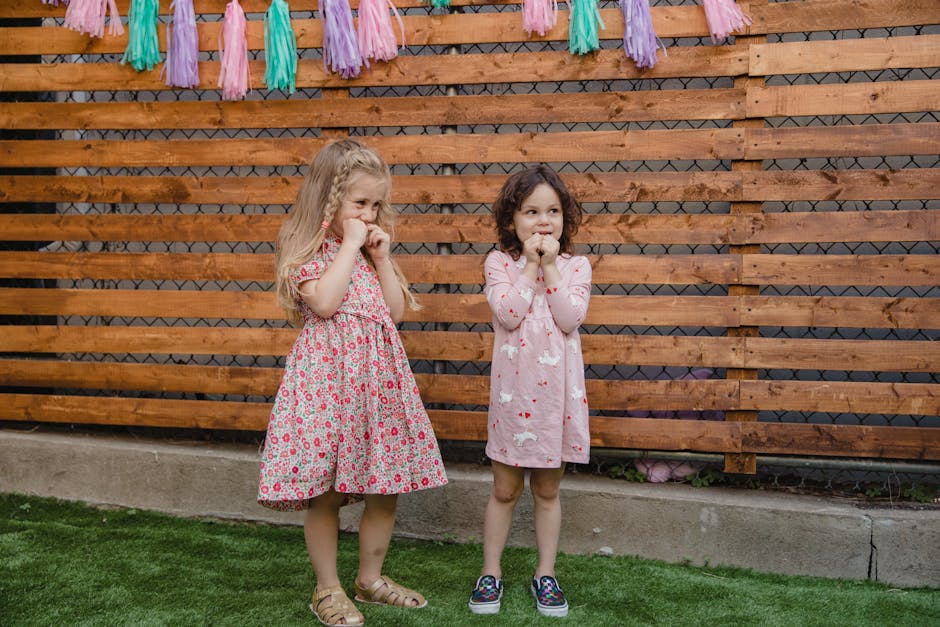 Two young girls standing playfully at a colorful outdoor birthday party.