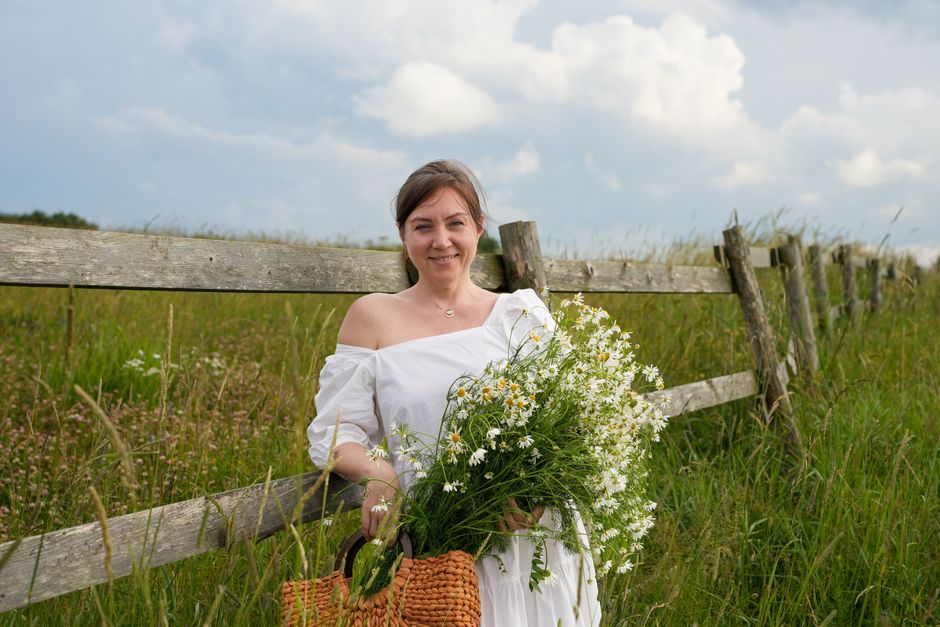 Woman holding daisies by a rustic fence on a sunny day in the countryside.