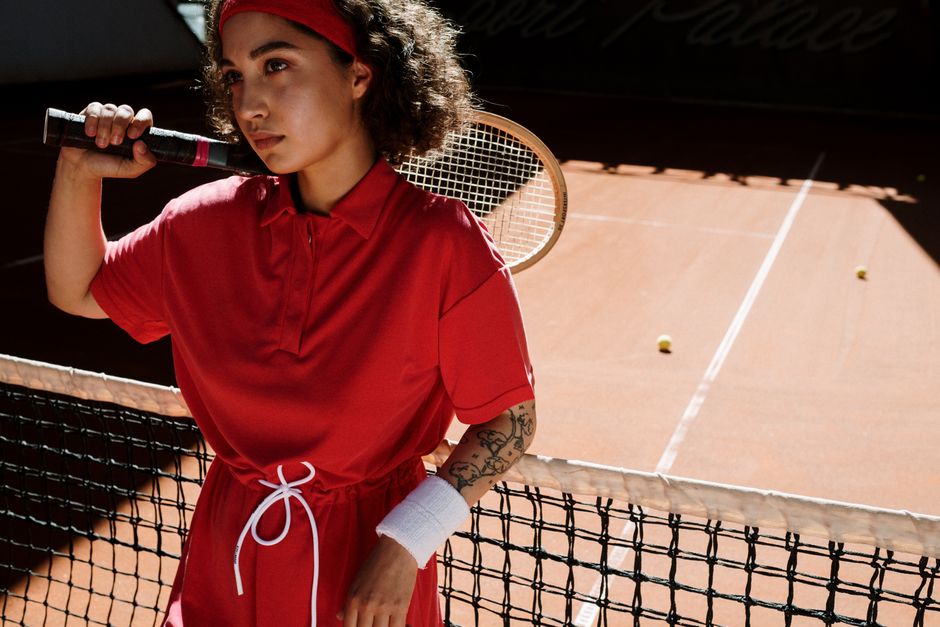 Stylish woman with curly hair holds a racket on a tennis court, exuding focus.