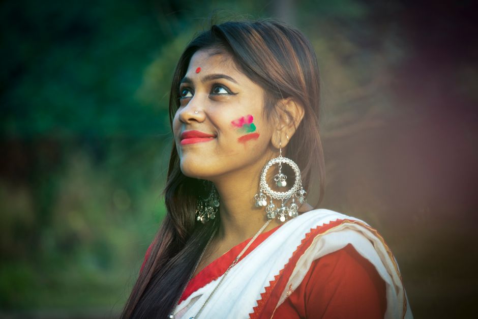 Portrait of a cheerful woman in a traditional saree with festive face paint, silver earrings, and a blurred background.