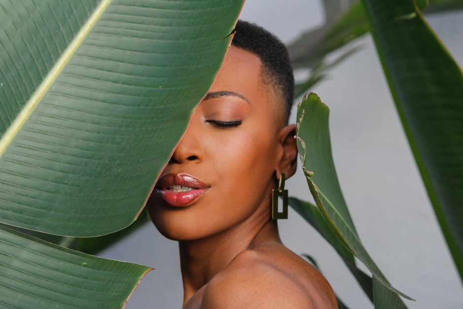 A serene portrait of a woman with closed eyes, framed by lush tropical leaves.