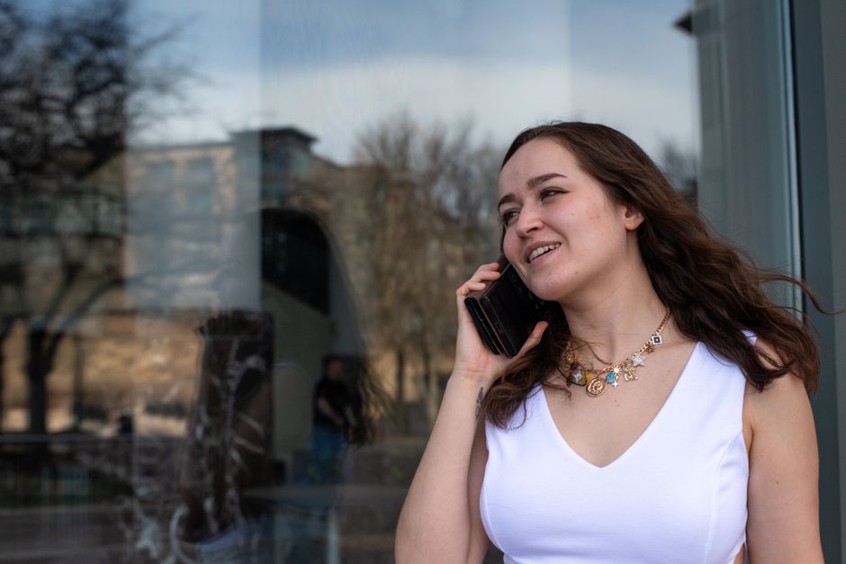 Young woman in a white dress talking on a smartphone, enjoying a sunny day outdoors.