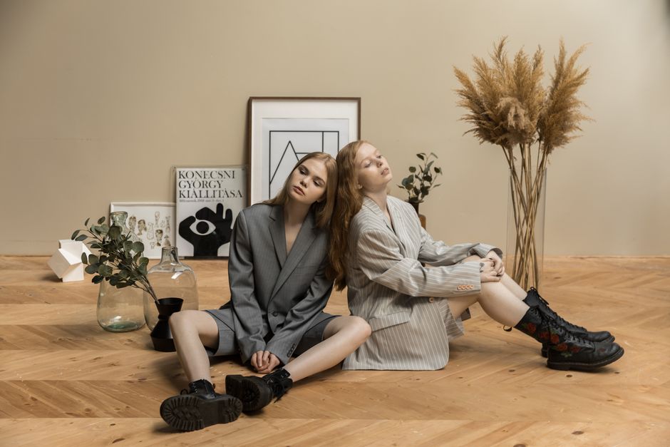 Two women in suits pose artistically indoors with a minimalist style.