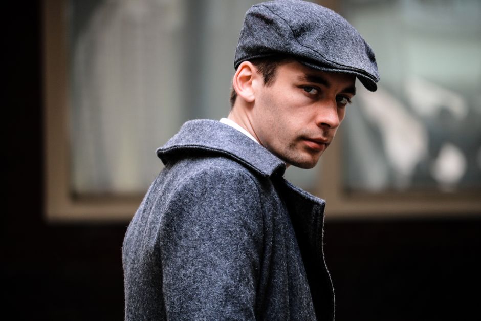 Portrait of a man in a gray coat and cap, looking stylish and fashionable outdoors.