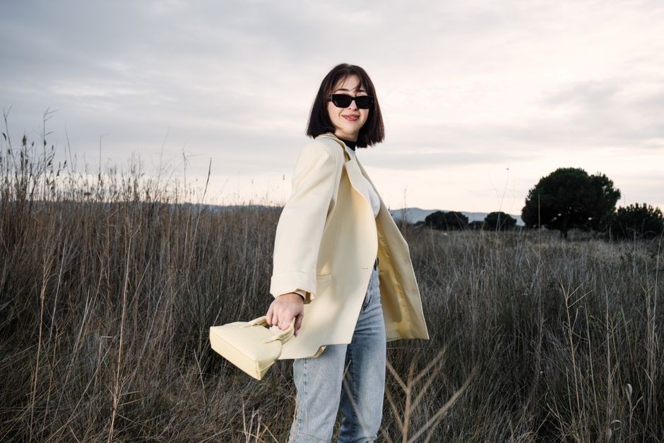 Fashionable woman in sunglasses with handbag in natural field setting.