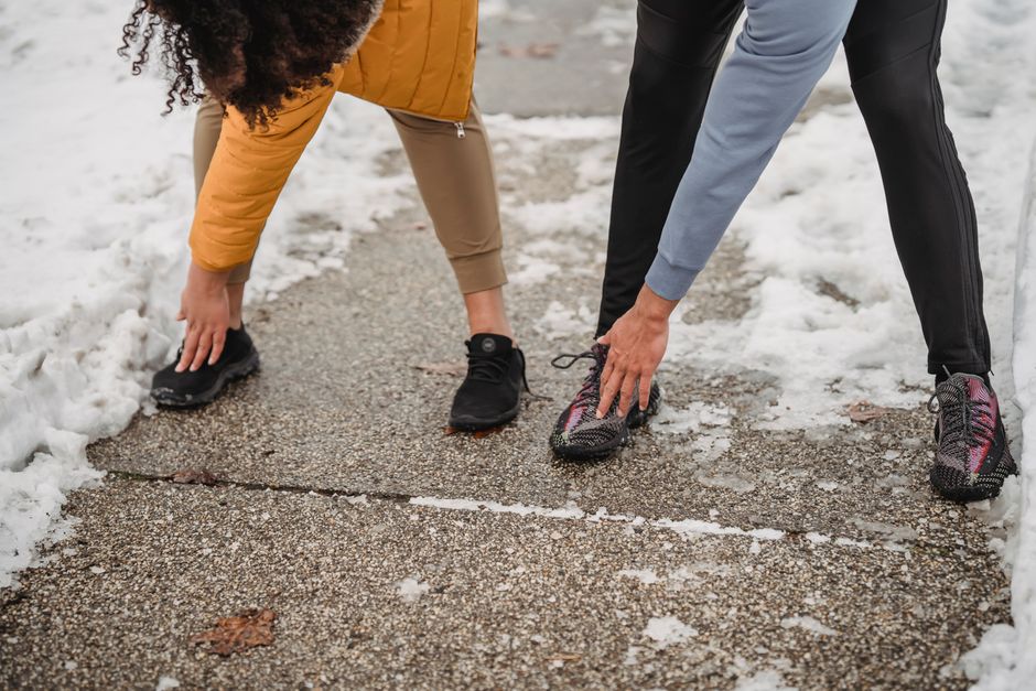 Crop unrecognizable sportspeople doing windmill arm exercise while training together on snowy walkway on clod winter day