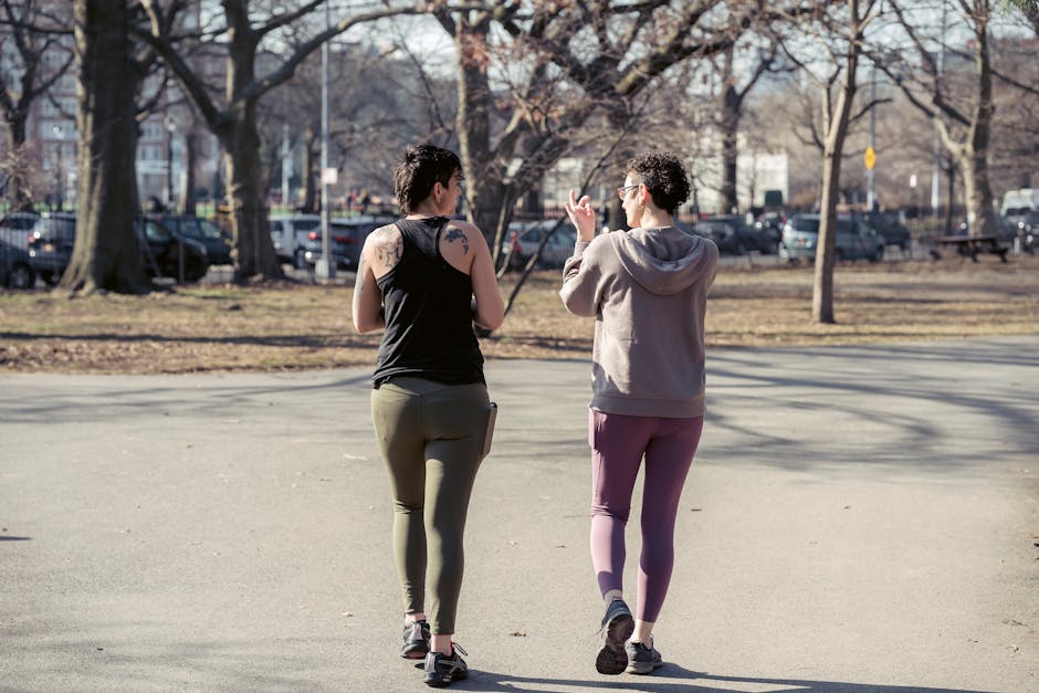 Back view full body sporty females in activewear strolling together in sunny autumn park and chatting
